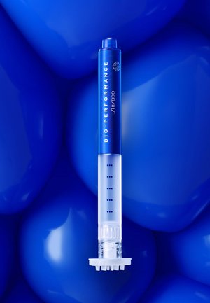 Blue cosmetic applicator with a transparent tip, featuring a patterned dispensing end and textured grip, labeled "BIO-PERFORMANCE."
