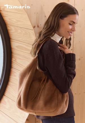 Sac à main en fausse fourrure marron avec une forme décontractée et des anses en cuir. Placé devant un fond en bois, le design présente des accents minimalistes.