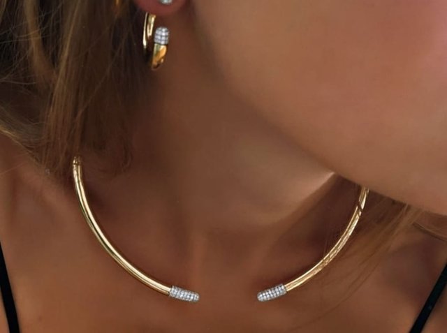 Χρυσή μεταλλική αλυσίδα με καμπυλωτό σχέδιο, με υφασμένους άκρους διακοσμημένους με μικρούς, διάφανους πολύτιμους λίθους. Ορατές χρυσές κρίκοι σκουλαρίκια που ταιριάζουν.