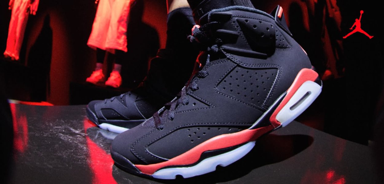 Zapatillas de baloncesto altas en negro y rojo usadas en interiores con iluminación roja y ropa colgada de fondo.