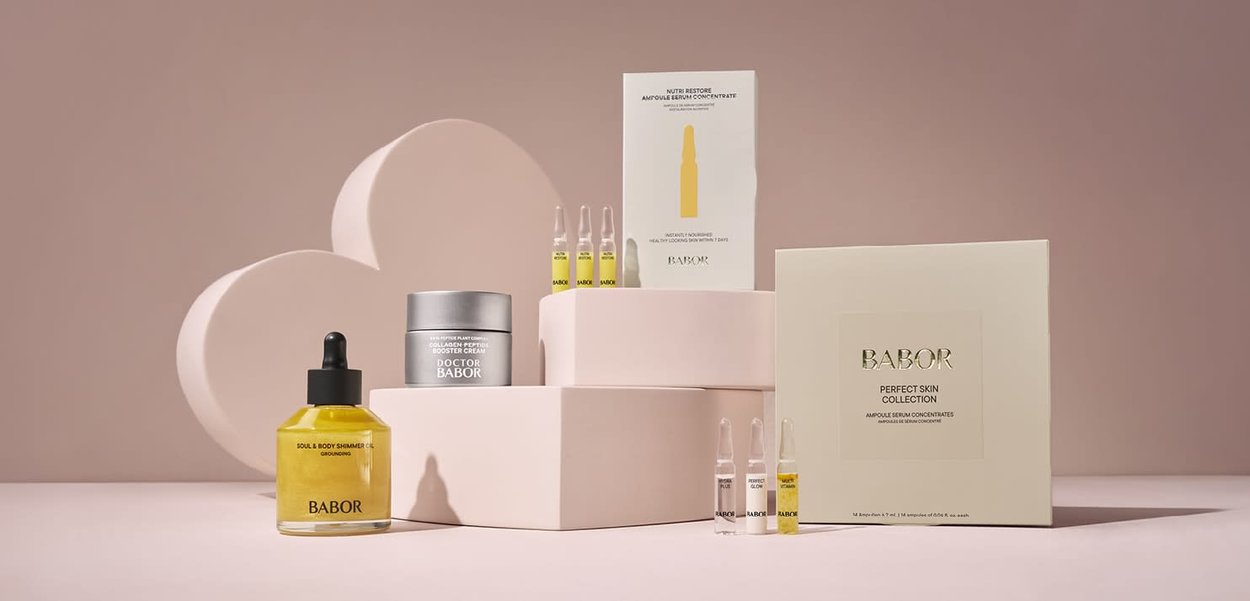 Produits de soin Babor comprenant des ampoules de sérum, une crème au peptide de collagène et une huile scintillante présentés sur des plateformes roses avec un fond en forme de cœur.