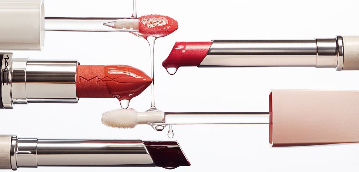 Vier lippenstiften in rode, oranje en donkere tinten met vloeibare druppels op de applicatoren en punten tegen een witte achtergrond.