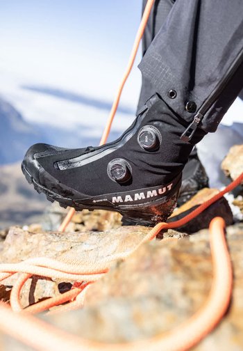 Schwarzer Gore-Tex Mammut-Kletterschuh mit Boa-Drehverschlüssen, getragen auf felsigem Gelände, gesichert mit einem orangefarbenen Kletterseil.