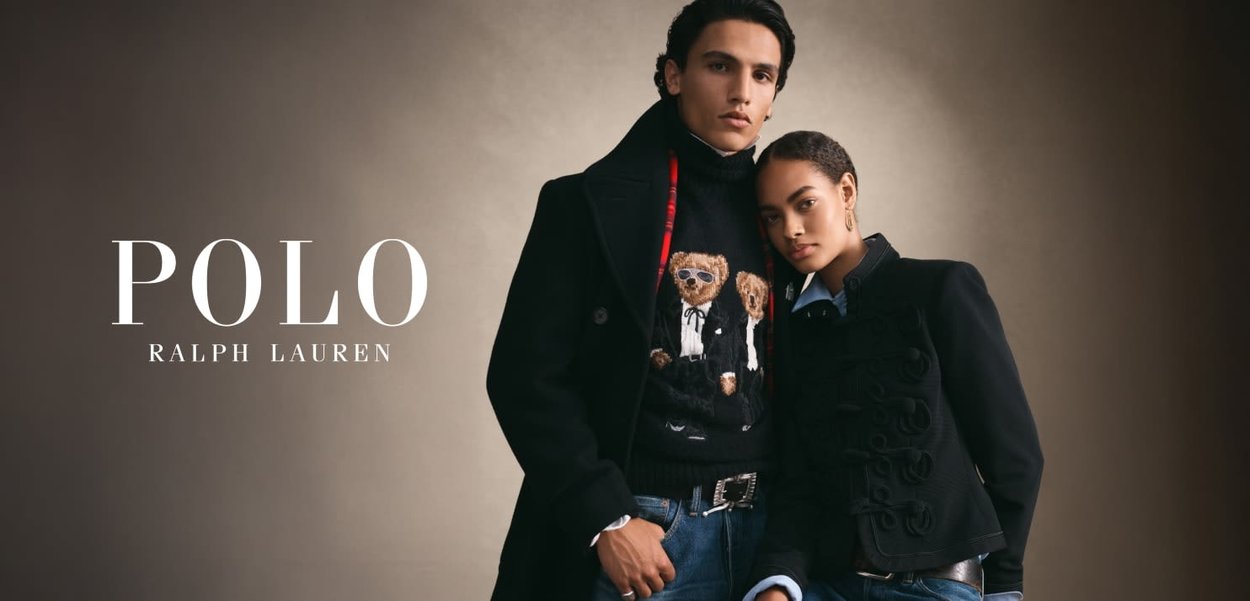 Two models wearing black jackets and sweaters, one with a teddy bear design, posing against a plain brown background.