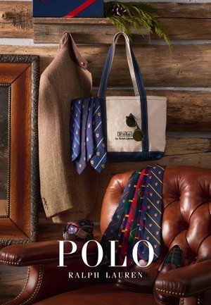 Canvas handlenett med marineblå aksenter, brun tweed-blazer, blå mønstrede slips og mørke solbriller på en skinnstol mot en rustikk bakgrunn.