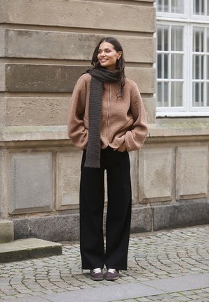 Brown fleece zip-up top with balloon sleeves, paired with black wide-leg pants and a dark striped scarf. Grey sneakers complete the outfit.