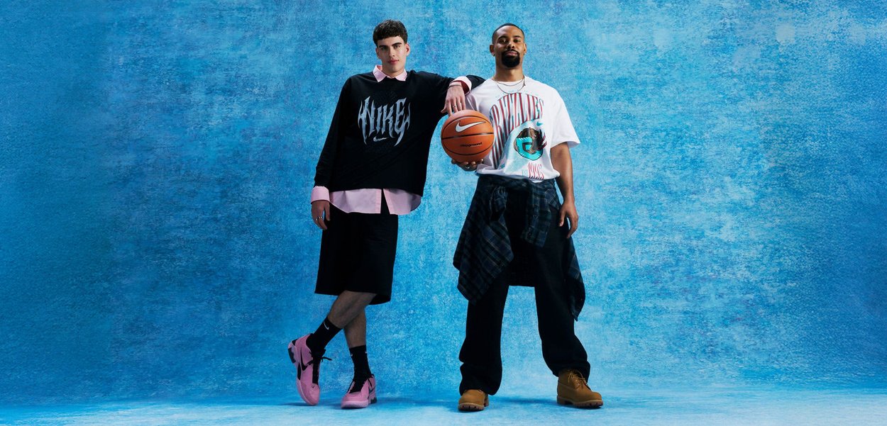 Twee mannen staan voor een blauwe achtergrond; de een draagt een Nike-trui en roze schoenen, de ander houdt een basketbal vast en draagt een Grizzlies-shirt en laarzen.