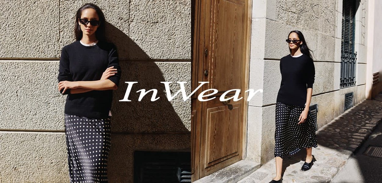 Schwarzer Strickpullover mit weißem Kragen, kombiniert mit einem schwarz-weiß gepunkteten Midirock. Glatter Stoff, lässige Passform, getragen mit schwarzen Schuhen.