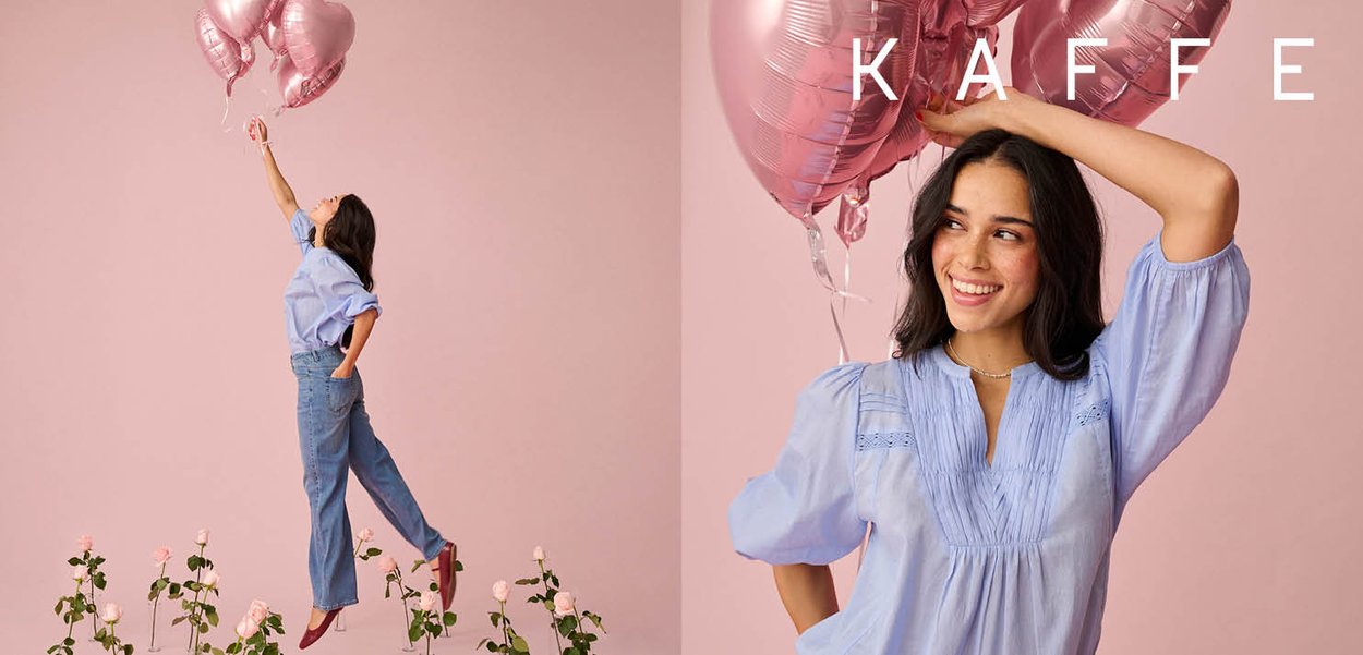 Frau in blauer Bluse und Jeans hält rosa herzförmige Luftballons und steht zwischen rosa Rosen vor einem blassrosa Hintergrund mit dem Schriftzug "KAFFE".