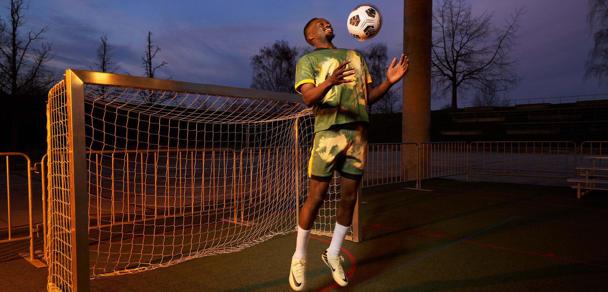 Grünes und gelbes gemustertes Sportoutfit mit einem kurzärmeligen Oberteil und Shorts, kombiniert mit weißen Socken und hellgelben Turnschuhen, in einer Sportumgebung.