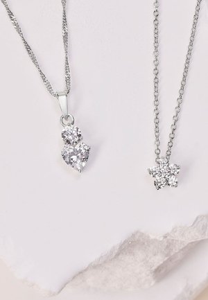 Deux colliers exposés sur un fond clair. L'un présente un pendentif en forme de cœur et un cristal rond sur une chaîne en argent ; l'autre arbore un design en cristal en forme d'étoile.