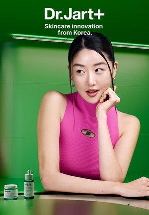 Les produits de soin de la peau Dr. Jart+ présentent une bouteille cylindrique verte et un pot blanc affichés sur une surface claire, devant un fond vert vif.