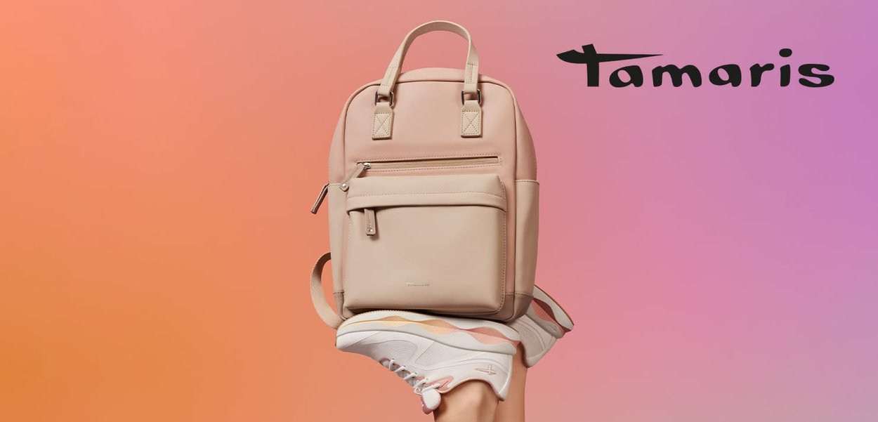 Beige backpack with two shoulder straps, a front zipper pocket, and smooth texture. Positioned above a foot wearing white sneakers with colorful accents.