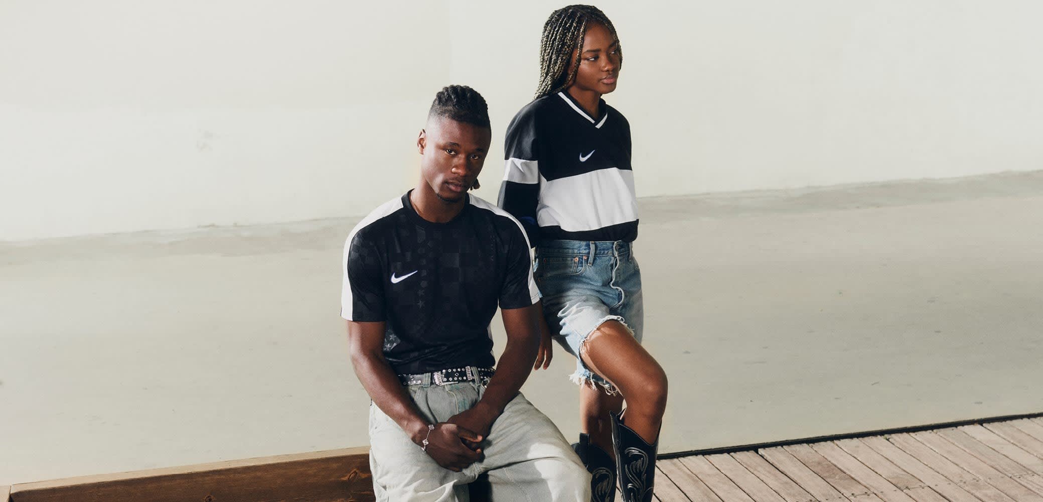 Camiseta gráfica negra de Nike en un modelo masculino, combinada con jeans de denim claros. Modelo femenino con una camiseta de rayas en blanco y negro de manga larga y pantalones cortos deshilachados.