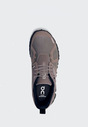 Zapato de senderismo impermeable marrón con suela negra, cordones y logo en la lengüeta, visto desde arriba sobre un fondo blanco.