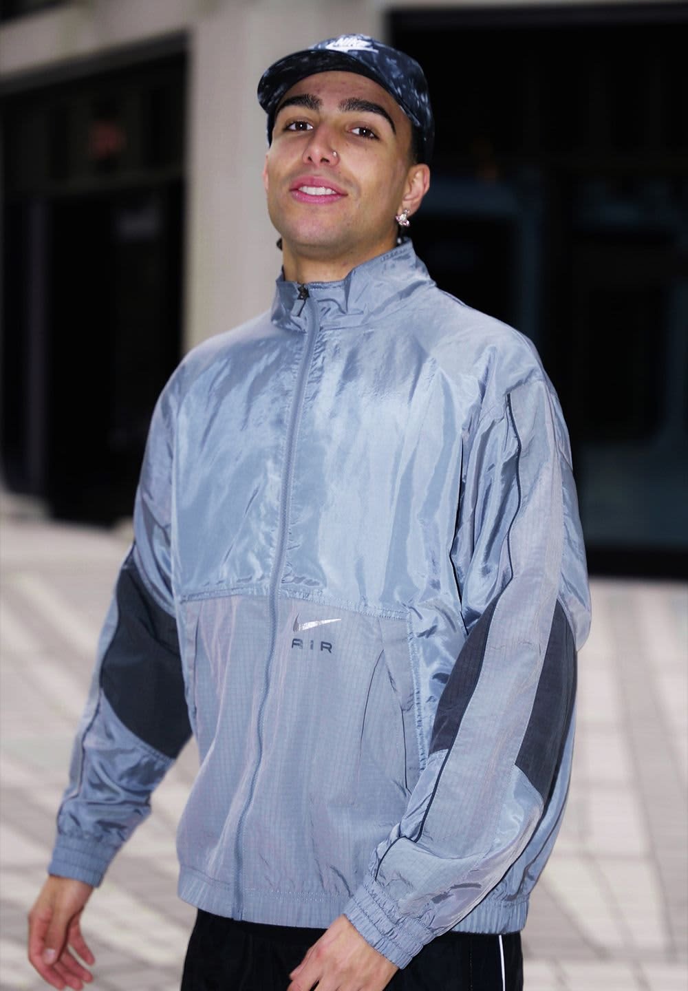 Silver windbreaker jacket with black accents, zip front, visible brand logo, and elastic cuffs. Features a shiny, textured finish.