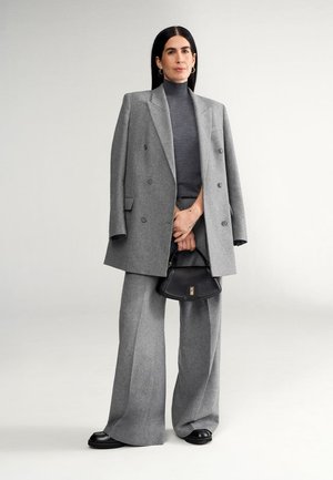 Blazer de lana gris de doble botón, suéter de cuello alto gris, pantalones anchos grises, bolso de piel negro y mocasines negros. Textura suave y ajuste a medida.