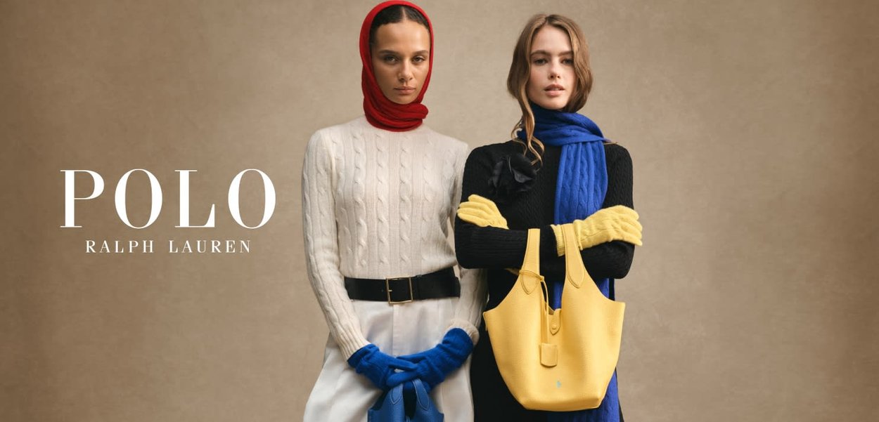 To modeller iført vinterklær. En i en kremfarget kabelstrikkegenser med et rødt skjerf, den andre i en svart kabelstrikk med et blått skjerf, holding en gul veske.