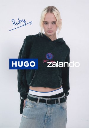 Schwarzer, kurzer Hoodie mit grafischem Design, kombiniert mit einem hellblauen Denim-Rock und einem schwarzen Gürtel. Weißer Bund mit blauen Akzenten.