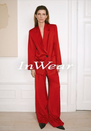 Roter maßgeschneiderter Anzug mit einem doppelt-reihigen Blazer und weiten Hosen. Glattes Material, strukturiertes Design, schwarze Knopfdetails, schlanke Silhouette.