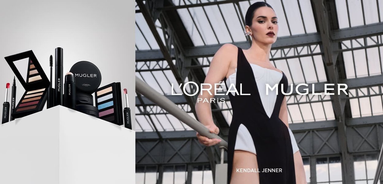 Produkty do makijażu L'Oréal Mugler ułożone na białym podeście; w skład wchodzą palety cieni do powiek, pomadka i tusz do rzęs w eleganckim czarnym opakowaniu.
