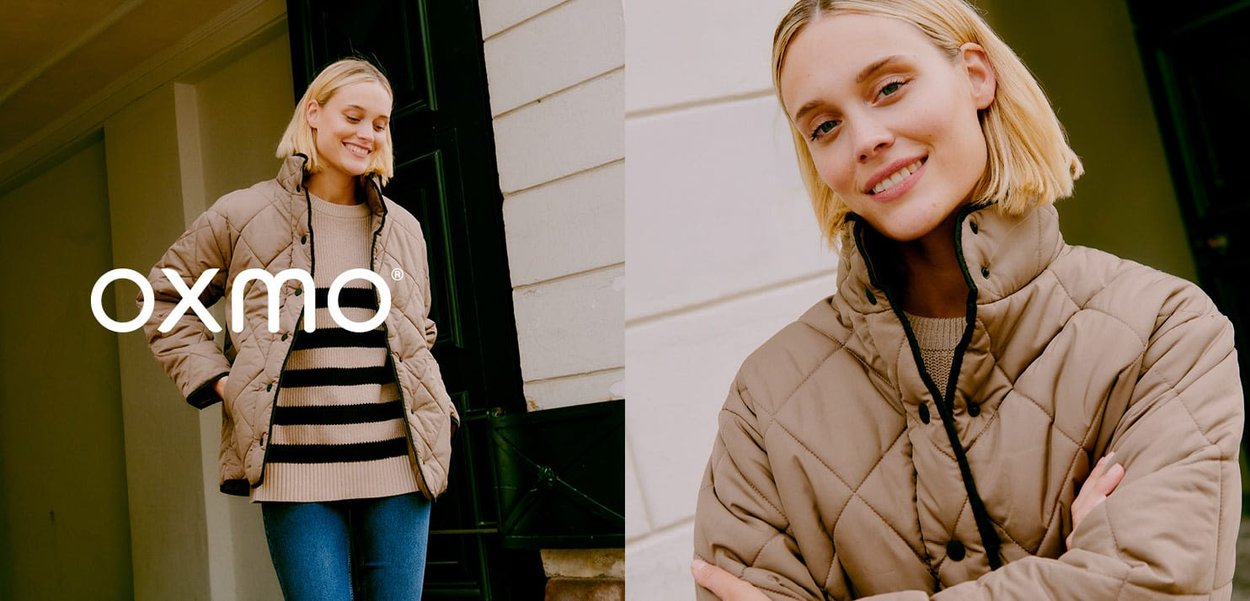 Veste beige matelassée avec col haut, présentant des accents et boutons noirs. Portée par-dessus un pull rayé, associée à un jean bleu.