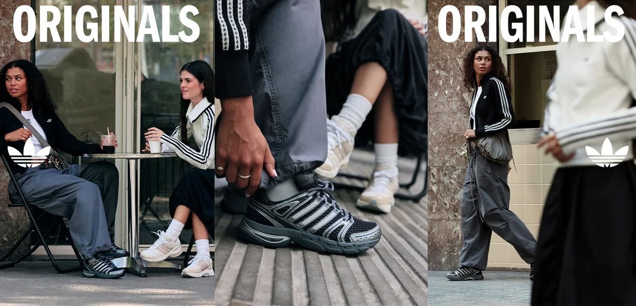 Scarpe da ginnastica nere e grigie con dettagli in rete e gomma, indossate con pantaloni jogger grigi e una giacca a righe bianca e nera in un caffè all'aperto.