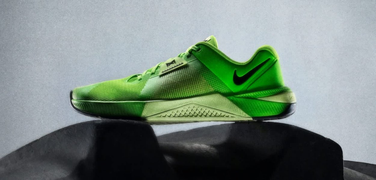 Scarpa da ginnastica Nike verde brillante con logo swoosh nero in equilibrio su uno pneumatico nero contro uno sfondo grigio chiaro.