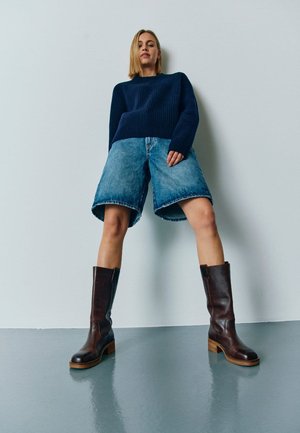 Marine ribbet sweater, denim shorts med løs pasform og mørkebrune knæhøje støvler med en kraftig hæl og struktureret finish.