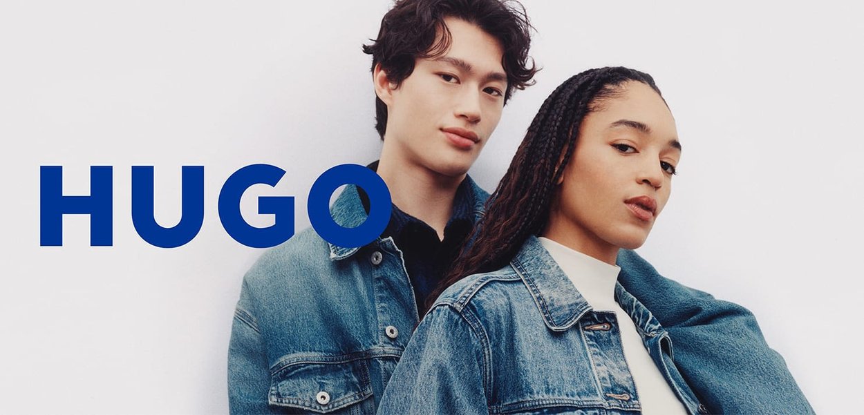 Twee jonge modellen in spijkerjacks poseren zelfverzekerd tegen een witte achtergrond met "HUGO" in vette blauwe letters.