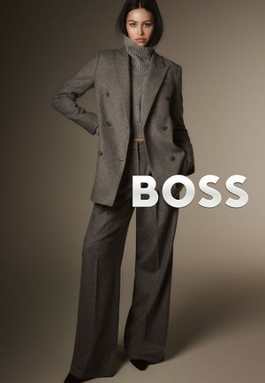 Blazer grigio doppiopetto con maglione a collo alto e pantaloni a gamba larga, tutti in un tessuto di lana texturizzata. Sovrapposizione audace del testo "BOSS".