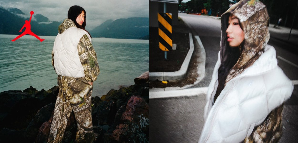 Frau in Tarnjacke und -hose mit weißer wattierter Weste, die am felsigen Ufer steht und mit hochgezogener Kapuze an der Straße entlanggeht, unter bewölktem Himmel.