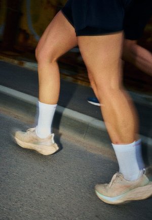 To personer løber på en asfalteret vej iført shorts, hvide sokker og beige løbesko, fotograferet fra knæene og ned.