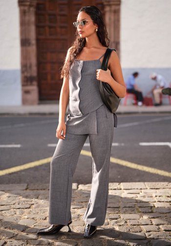 Siva majica bez rukava s valovitim donjim rubom, u kombinaciji s labavim hlačama u istoj boji. Odjeća ima tanke naramenice i strukturiranu tkaninu. Crne cipele s visokom petom.