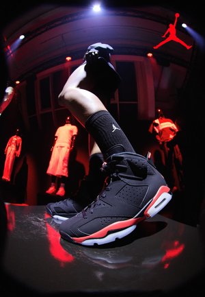 Persona che indossa scarpe da ginnastica Air Jordan nere e rosse e calzini Jordan neri, con manichini illuminati da luce rossa sullo sfondo in un locale buio.