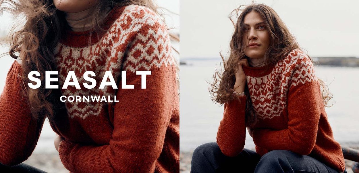 Roter gestrickter Pullover mit weißem Muster an der Schulterpartie, ausgestattet mit einem gerippten Rundhalsausschnitt und strukturierter Oberfläche, kombiniert mit dunklen Hosen.