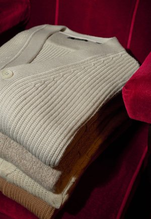 Stapel aus drei gestrickten Cardigans in Off-White, Beige und Hellbraun mit gerippter Struktur und einem einzelnen Knopfverschluss.