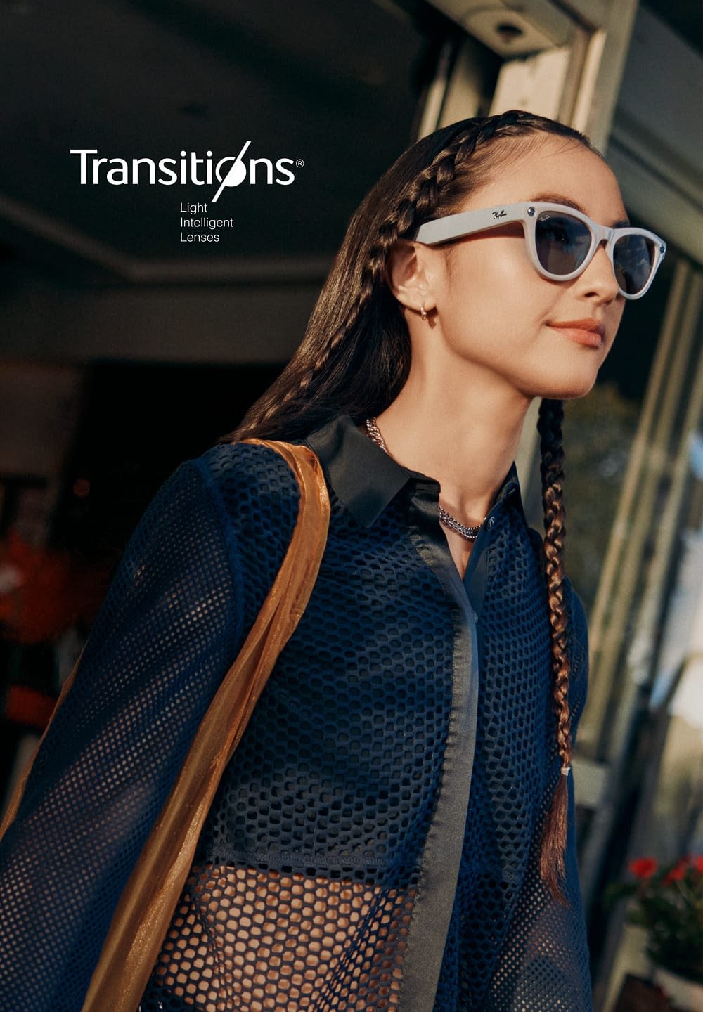 Lunettes de soleil avec une monture et des verres clairs. Le modèle porte une chemise en maille noire avec un col structuré et un sac à épaule marron.