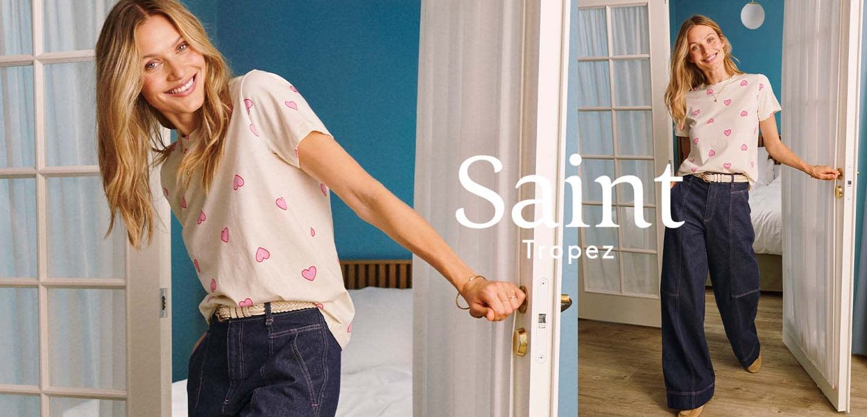 Lächelnde Frau in einem herzgemusterten Hemd und Schlagjeans, die weiße französische Türen in einem hellen, modernen Raum mit blauer Wand und Holzboden öffnet.