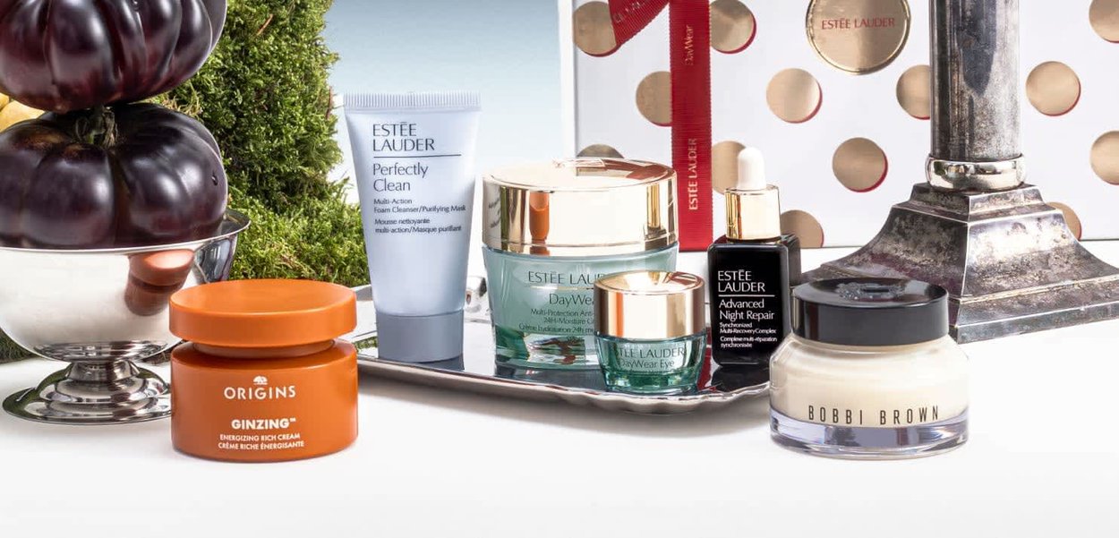 Produits de soin de la peau d'Origins, Estée Lauder et Bobbi Brown disposés sur un plateau avec des citrouilles décoratives et du feuillage.