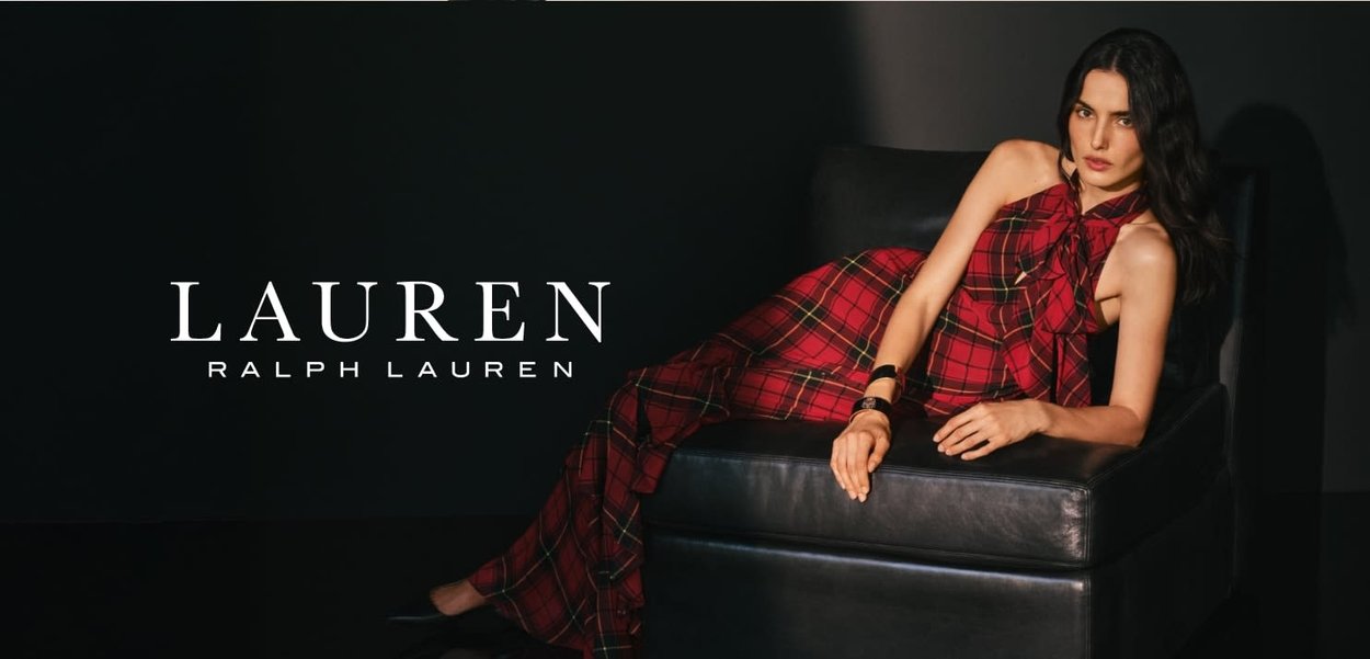 Rutete rød kjole med sløyfedetalj, båret av en modell som sitter på en svart skinnsofa, mot en mørk bakgrunn. "LAUREN RALPH LAUREN" merkevare.