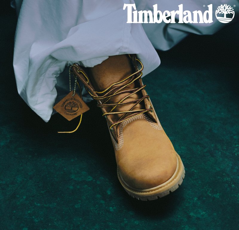 Brązowe skórzane buty Timberland z brązowymi sznurowadłami i metalowymi oczkami, z chropowatą podeszwą i okrągłą metką z logo przyczepioną do buta.