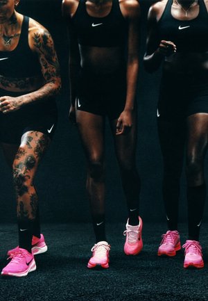 Calzado deportivo Nike en rosa, con materiales de malla y sintéticos. Tres atletas en ropa deportiva negra, mostrando tatuajes diversos y una complexión atlética.