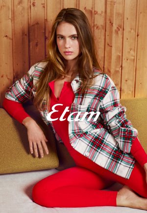 Czerwony body zestawiony z flanelową koszulą w kratę w kolorach białym, zielonym i czerwonym. Tło z drewna i żółta teksturowana poduszka.