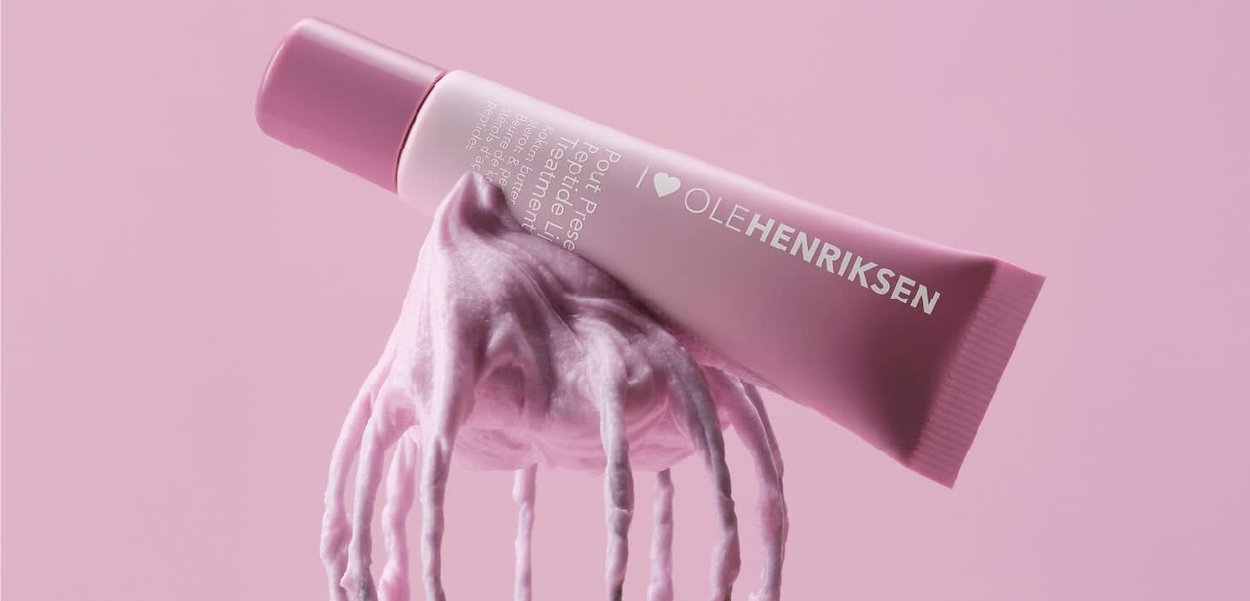 Tube de soin rose Ole Henriksen avec de la crème qui s'en écoule et coule sur un fond rose assorti.