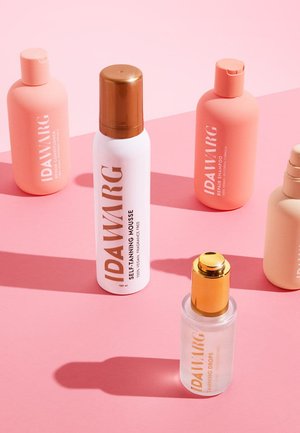 Cinq flacons de soins IDA WARG sur une surface rose : pêche mat, blanc avec un capuchon doré, et transparent avec des accents dorés, présentant un design minimaliste et du texte.