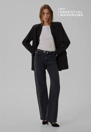 Blazer noir sur un haut blanc côtelé, associé à un jean gris foncé à jambes larges. Talons noirs complètent la tenue. Détails minimalistes et lignes épurées.
