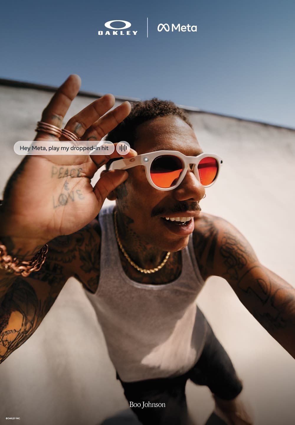 Occhiali da sole bianchi con lenti tinte di rosso, montatura rotonda e un motivo discreto. Uomo che gesticola con una mano, indossa una canottiera grigia e gioielli.