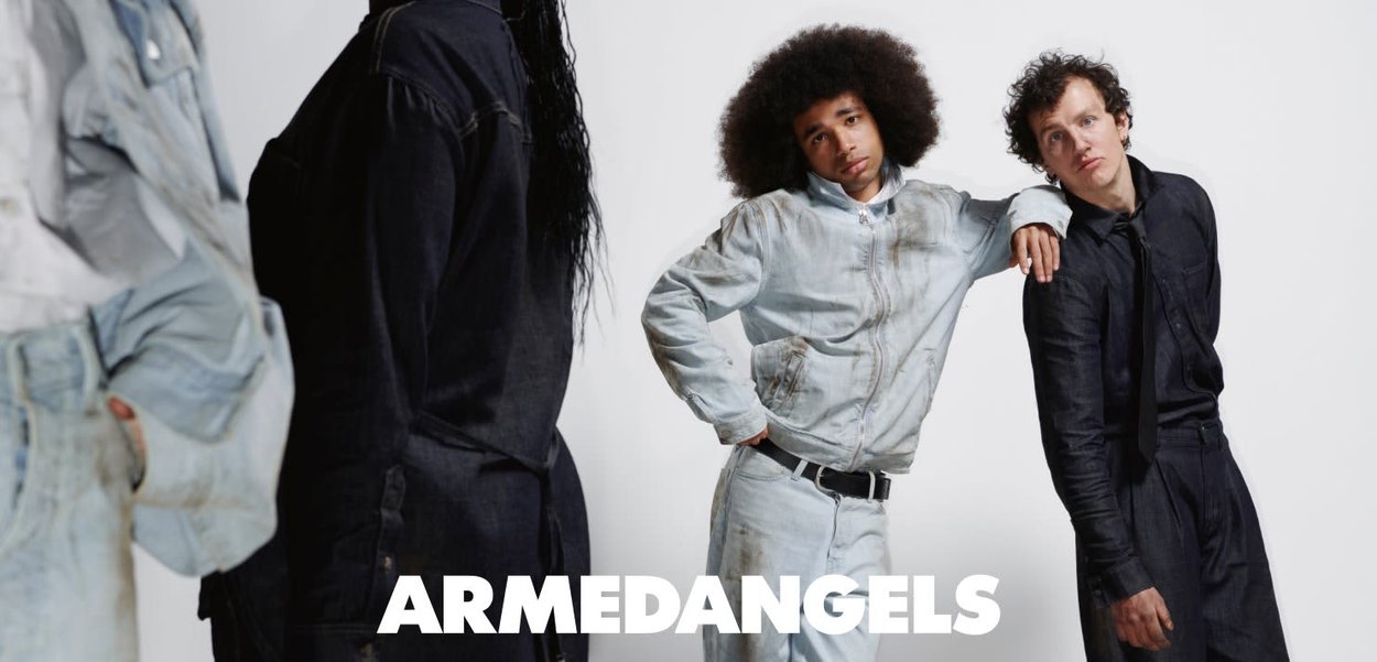 Zwei Männer in legerer schwarzer und heller Denim-Kleidung posieren selbstbewusst vor einem weißen Hintergrund mit dem Schriftzug "ARMEDANGELS" darunter.