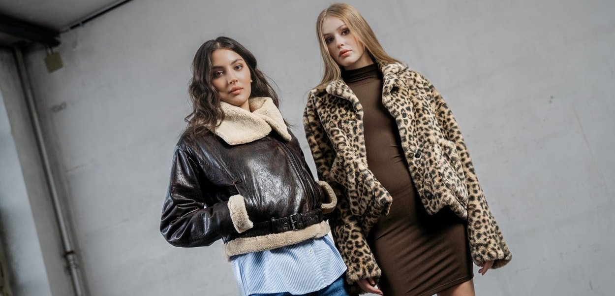 Due donne che indossano capispalla: una giacca di pelle marrone con colletto in shearling crema e un cappotto di pelliccia sintetica leopardata. Entrambe sono presentate con stile.